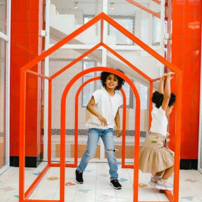 Two kids having fun inside a modern red frame playhouse at indoor playground.