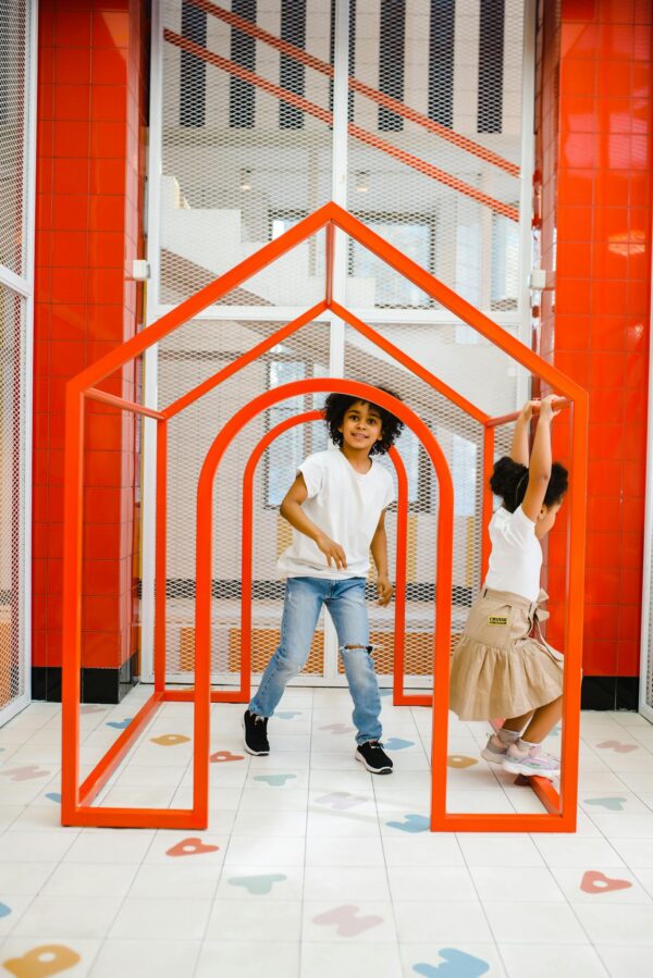 Two kids having fun inside a modern red frame playhouse at indoor playground.